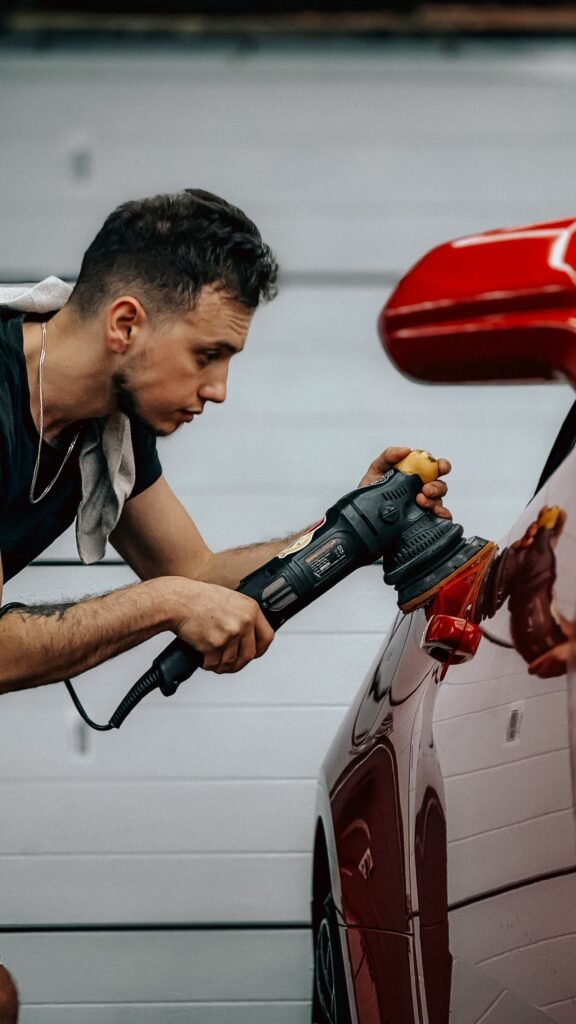Detailer machine polishing the panel of a red car in a workshop